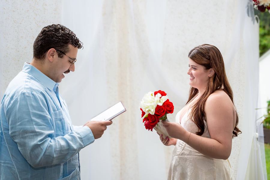 A man reads a heartfelt note to his partner, who holds a bouquet of red and white roses